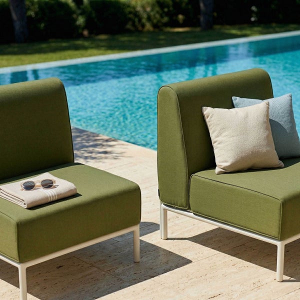 Moderne Garten-Loungesessel mit Textilpolsterung und Metallrahmen auf einer Steinterrasse an einem Pool.