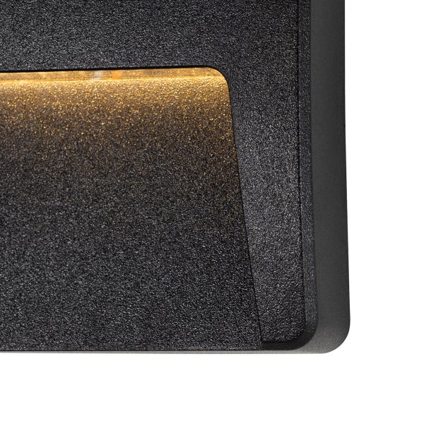 Nahaufnahme einer schwarzen, texturierten Wandleuchte mit warmweißem Lichtschein aus einer Aussparung.