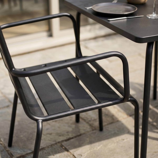 Gartenstuhl aus Metall mit Sitzlatten neben einem Gartentisch auf einer Terrasse.