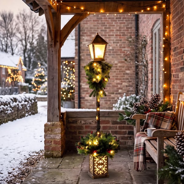 Weihnachtliche Laterne als Dekosäule mit LED Beleuchtung und Tannengrün auf einer winterlichen Veranda.