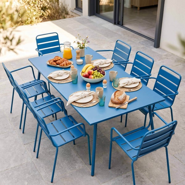 Moderner blauer Gartentisch mit acht passenden Armlehnstühlen aus Metall auf einer hellen Terrasse, eingedeckt für ein Frühstück.