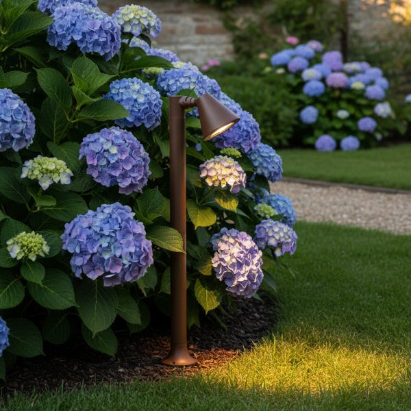 Braune Garten-Wegeleuchte beleuchtet blaue Hortensien in einem gepflegten Garten.