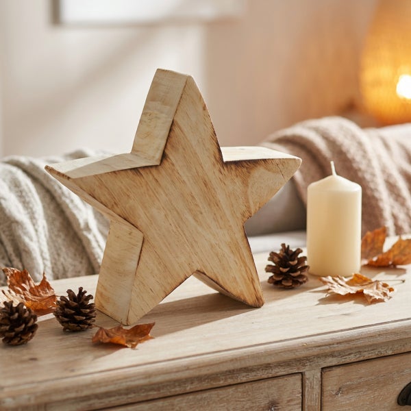 Dekorativer Holzstern als herbstliche Tischdekoration mit Kerze und Kiefernzapfen auf einer Kommode.