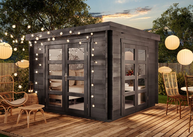 Modernes Gartenhaus aus dunklem Holz mit Flachdach und großen Glasdoppeltüren auf einer Holzterrasse mit dekorativer Beleuchtung.