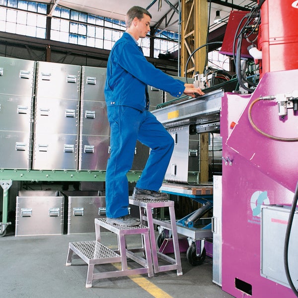 Mann auf dreistufiger Aluminiumleiter, der an einer Maschine arbeitet, im Hintergrund Metallkisten
