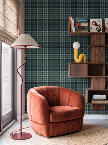 Wohnzimmer mit grün-blau-weiß karierter Tapete, einem orangefarbenen Sessel, einer Stehleuchte und einem Wandregal aus Holz.
