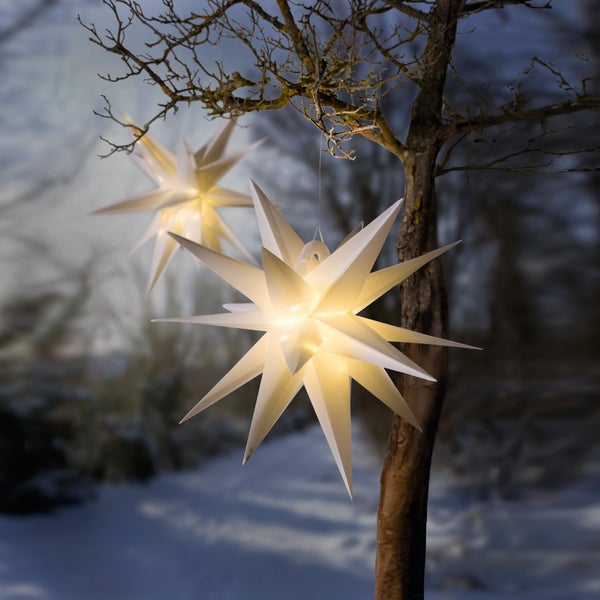 Zwei beleuchtete Papiersterne hängen an einem Baum im Winter.