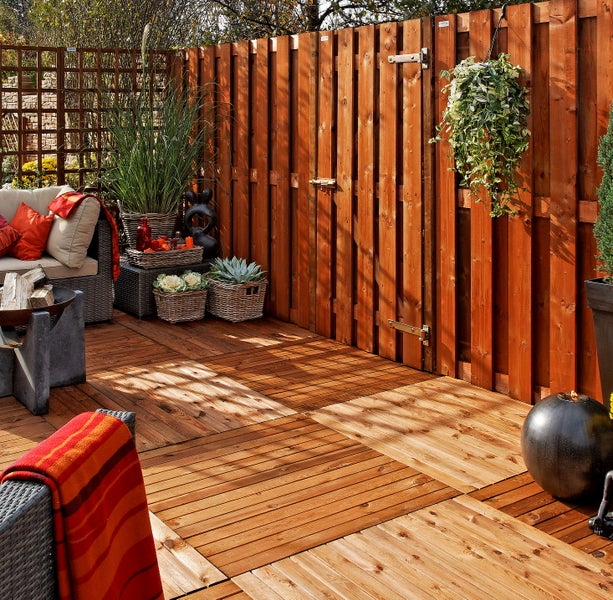 Terrassenfliesen aus Holz und ein Sichtschutzzaun auf einer hellen, organisierten Terrasse mit Gartenmöbeln und Pflanzen.