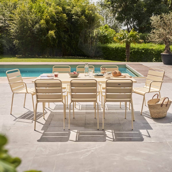 Gartenmöbel-Set mit großem Esstisch und acht Stühlen aus Metall auf einer Terrasse an einem Pool in einem hellen Garten.