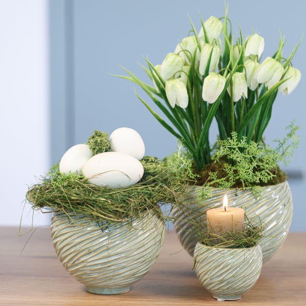 Dekorative Osterarrangements mit Eiern, Blumen und Kerze in passenden Gefäßen