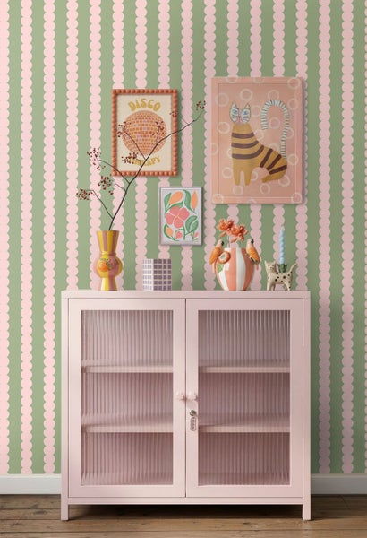 Tapete mit Punktemuster, rosa Vitrinenschrank mit Riffelglas, Dekovasen und Wandbilder in einem hellen, farbenfrohen Raum im Retro-Stil.