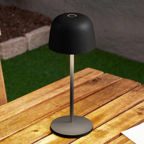 Moderne schwarze LED-Tischleuchte für den Außenbereich auf einem Holztisch in einem Garten.