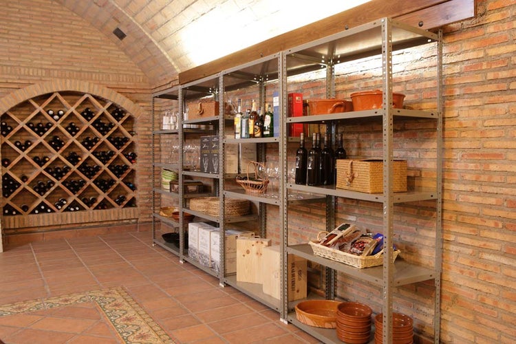 Geräumiger Keller mit Backsteinwänden und Metallregalen zur Lagerung von Flaschen, Körben und Boxen. Im Hintergrund ein bogenförmiges Weinregal.