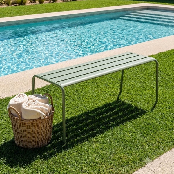 Grüne Gartenbank aus Metall mit Lattenstruktur auf einem Rasen neben einem Pool, inklusive eines geflochtenen Korbs mit Handtüchern.