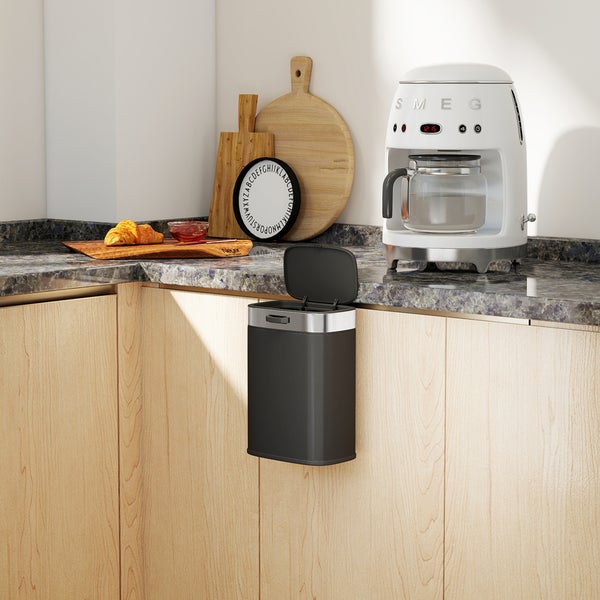 Küchenszene mit einem an der Schranktür befestigten Mülleimer, einer SMEG Kaffeemaschine und Holzschneidebrettern.