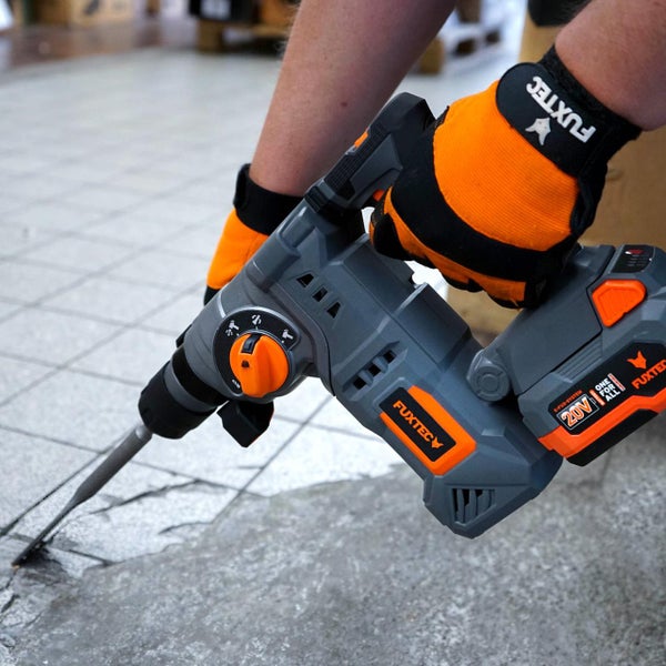 Eine Person benutzt einen akkubetriebenen Fuxtec Bohrhammer mit 20 Volt Akku zum Meißeln auf einem Fliesenboden.