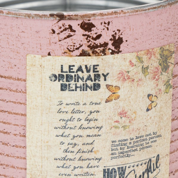 Dekorativer Übertopf aus Blech in Rosa mit Vintage Schriftzug Leave Ordinary Behind und floralen Mustern.