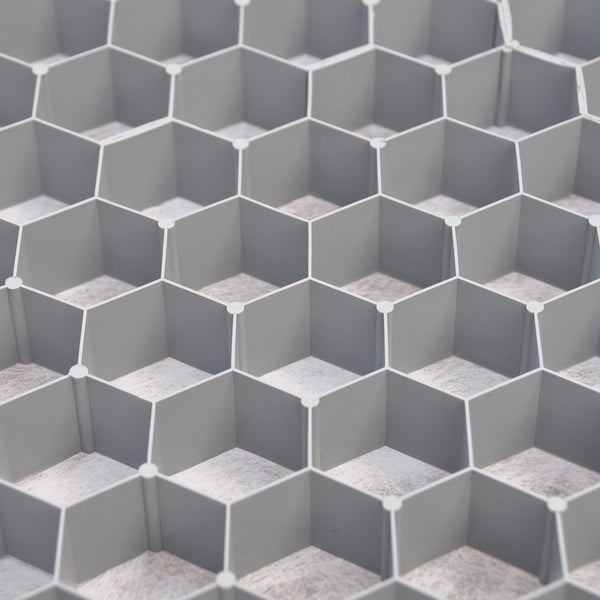 Nahaufnahme eines grauen Kiesgitters aus Kunststoff mit sechseckiger Wabenstruktur und integriertem Geotextilvlies zur Bodenstabilisierung.
