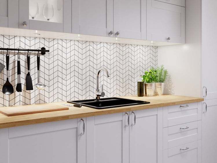 Helle Küche mit Arbeitsplatte aus Holz, schwarzem Einbaubecken, Chromarmatur und Fliesenspiegel im Fischgrätmuster.