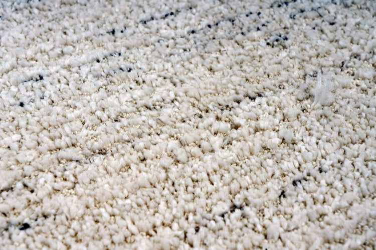 Nahaufnahme eines flauschigen Hochflor Teppichs mit strukturierter Oberfläche und eingewebten dunklen Akzenten.