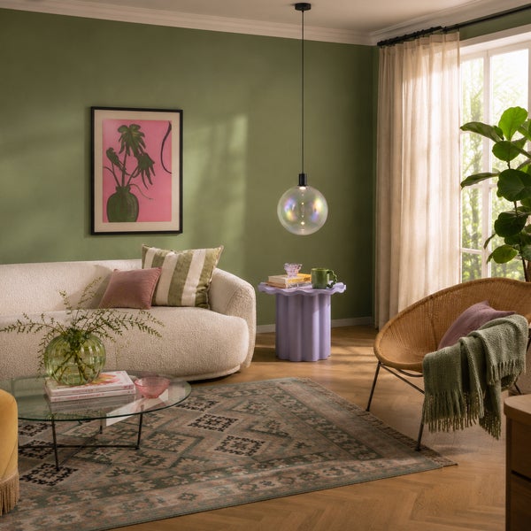 Modernes Wohnzimmer mit strukturiertem Sofa, rundem Couchtisch, Rattan-Sessel, Teppich und Pendelleuchte in einem hellen, gemütlichen Interieur.