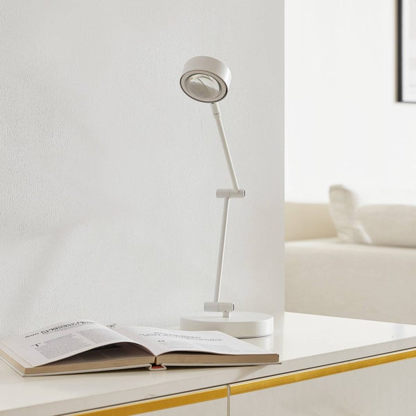 Weiße Schreibtischlampe neben einem offenen Buch auf einem Tisch