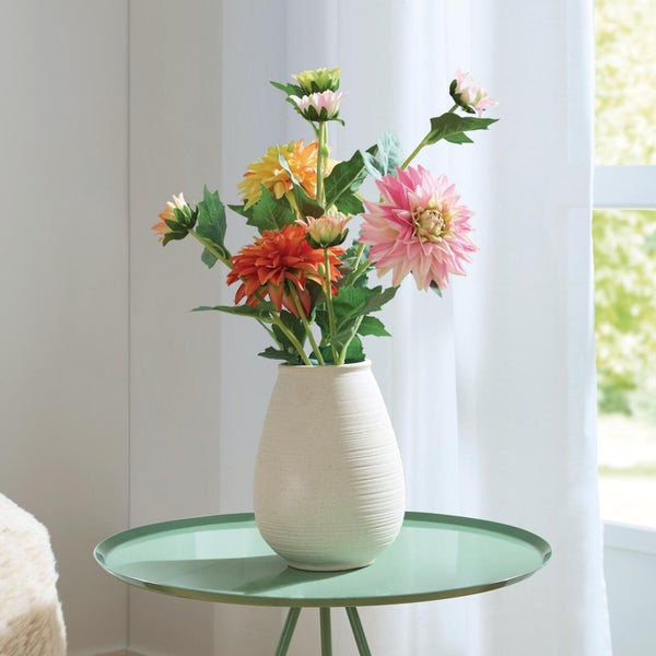 Künstliches Dahlien-Bouquet in einer strukturierten Keramikvase auf einem grünen Beistelltisch in einem hellen Raum.