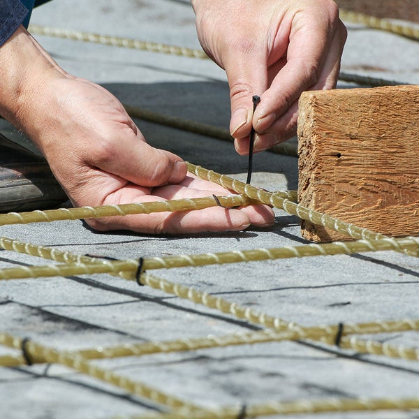 Detailaufnahme: Mann befestigt Bewehrungsstahl mit Kabelbinder an einem Holzstück.
