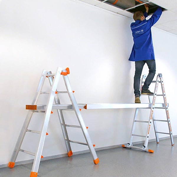 Handwerker arbeitet an einer Decke, stehend auf einer Aluminium Arbeitsbühne, die zwischen zwei Leitern gespannt ist.