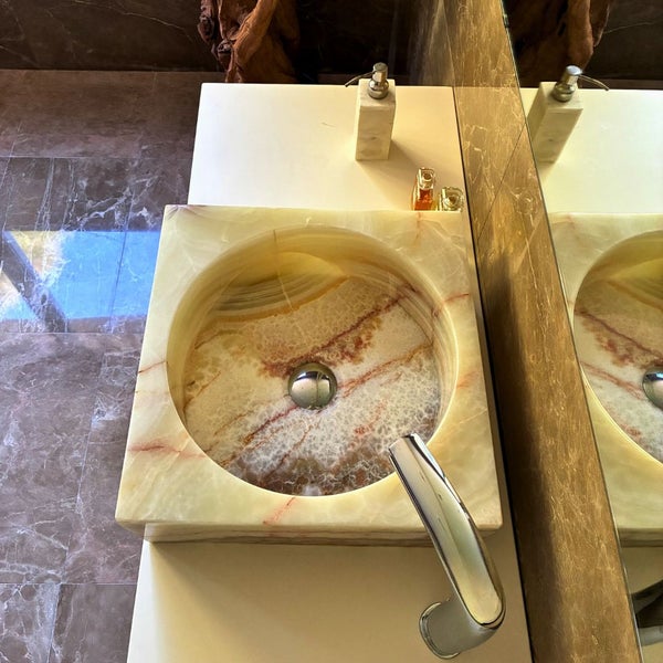 Quadratisches Aufsatzwaschbecken aus Naturstein mit runder Innenform auf einem Waschtisch in einem modernen Badezimmer.