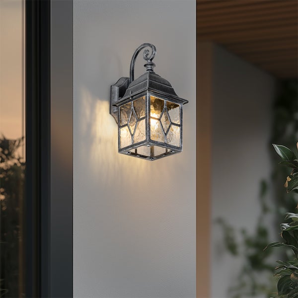 Klassische Außenwandleuchte in Laternenform aus Metall und Glas an einer Hauswand mit hellem, warmem Licht.