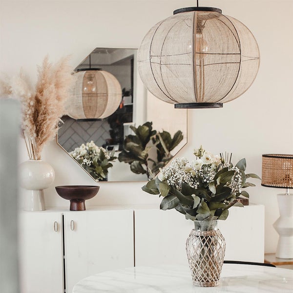 Pendelleuchte mit Stoffschirm in einem hellen, modernen Wohnbereich mit Spiegel, Sideboard und Blumendekoration.