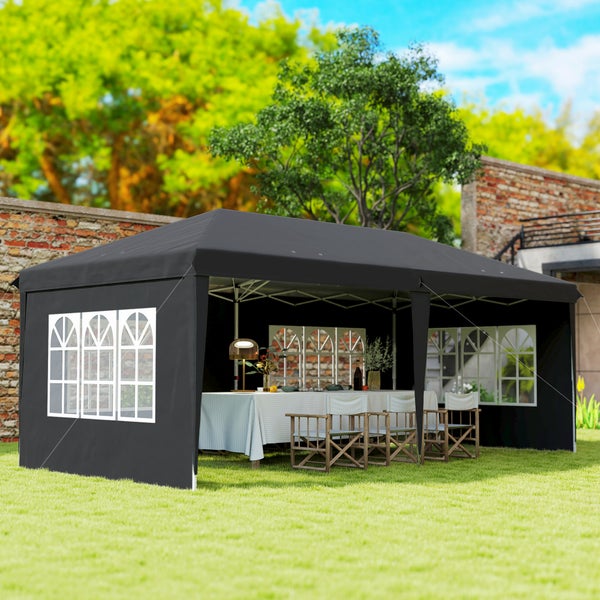 Schwarzer Gartenpavillon mit Seitenwänden und Fenstern auf einer Rasenfläche, innen ein gedeckter Tisch mit Stühlen.