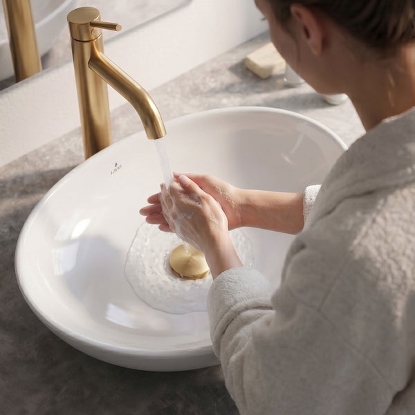 Händewaschen in einem weißen Lavio Aufsatzwaschbecken mit einer hohen goldfarbenen Armatur auf einer grauen Steinplatte in einem hellen Bad.