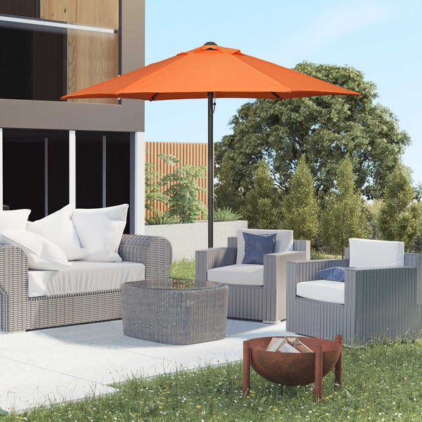 Großer orangefarbener Sonnenschirm über grauer Lounge-Garnitur aus Polyrattan auf einer Terrasse mit Sofa, Sesseln und Feuerschale.