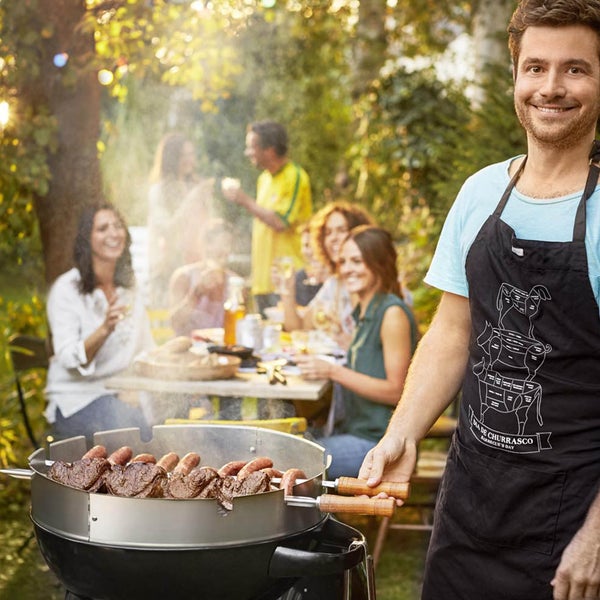 Szene mit einem Mann, der in einem Garten am Grill steht, mit Freunden im Hintergrund.