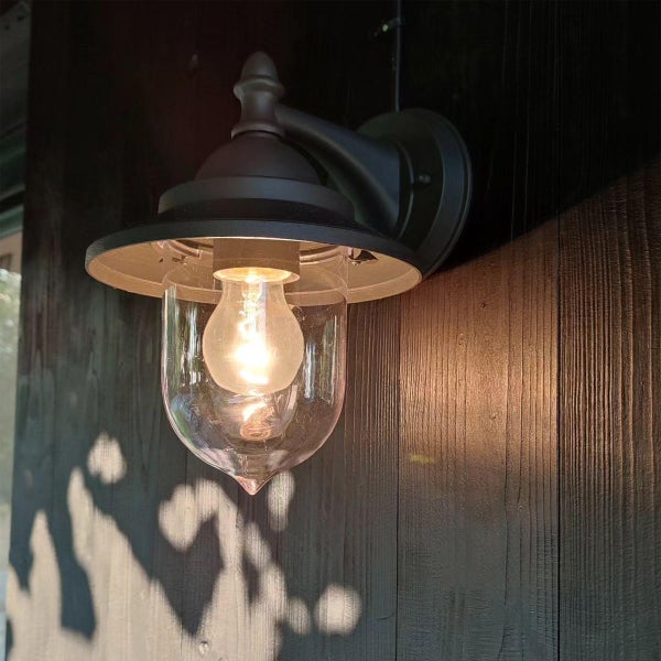 Außenwandleuchte mit klarem Glasschirm und Metallhalterung, montiert an einer Holzwand, mit brennendem Leuchtmittel.