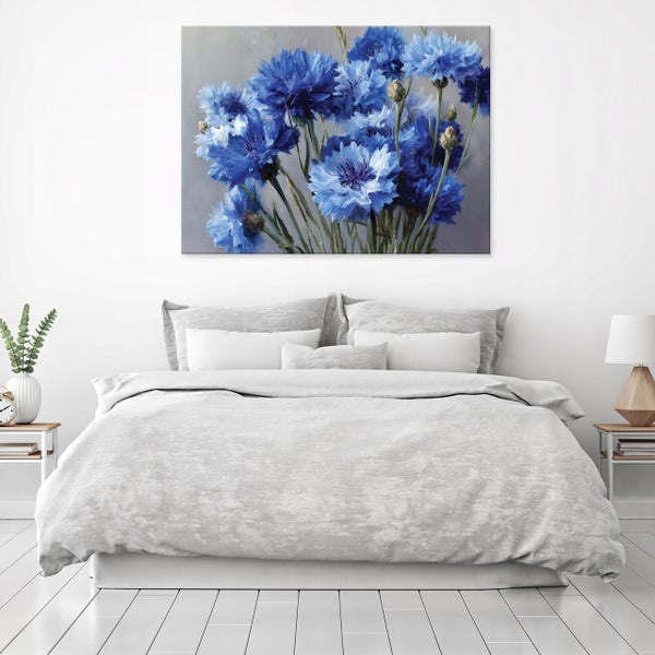 Wandbild mit blauen Kornblumen über einem Doppelbett in einem hell eingerichteten Schlafzimmer.