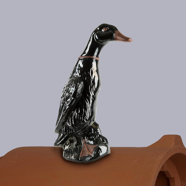 Schwarze Firstfigur Ente aus glasierter Keramik auf einem braunen Firstziegel montiert.