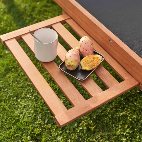 Gartenliege mit ausziehbarem Beistelltisch aus Holz, auf dem eine Tasse und Kaktusfeigen stehen, im Garten.