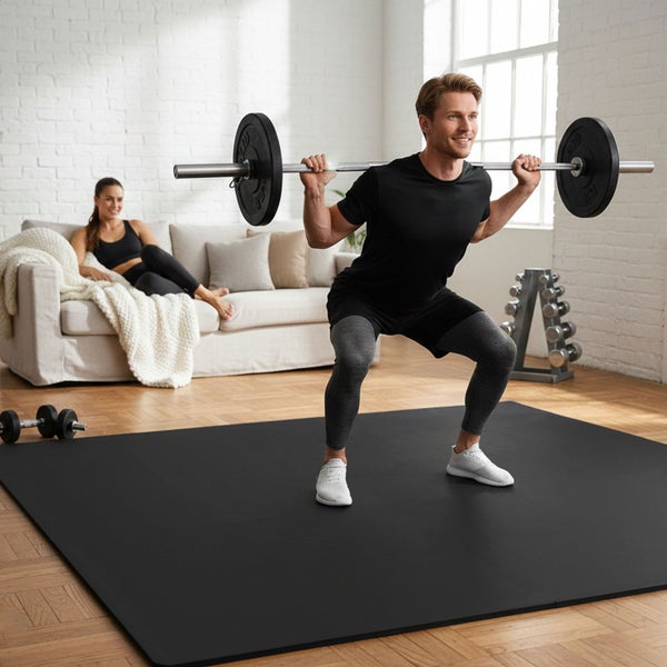 Mann macht Kniebeugen mit einer Langhantel auf einer Trainingsmatte in einem hellen Raum.