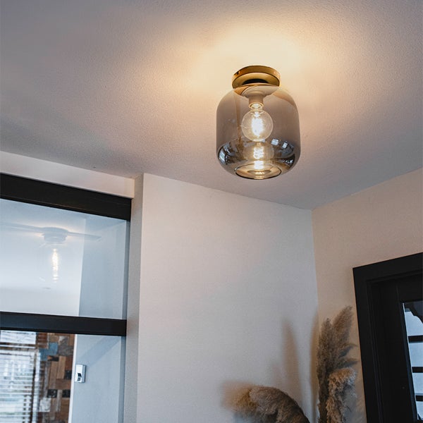 Moderne Deckenleuchte mit rauchfarbenem Glasschirm und messingfarbenem Sockel an einer Decke montiert.