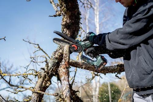 Eine Person benutzt eine Akku-Astsäge der Marke Metabo, um einen Ast zu sägen.