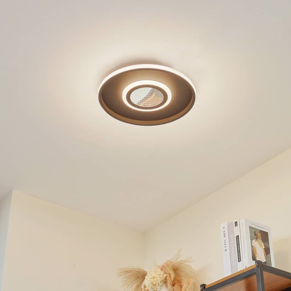 Runde Deckenleuchte mit konzentrischen Leuchtringen montiert an einer weißen Decke in einem hellen Raum über einem Bücherregal.