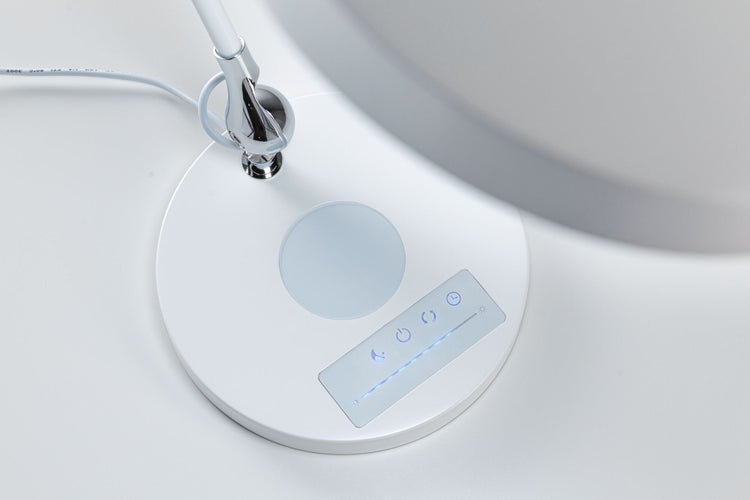 Sockel einer weißen Schreibtischleuchte mit Touch-Bedienfeld für Helligkeit, Farbtemperatur und Timer sowie integrierter Ladestation.