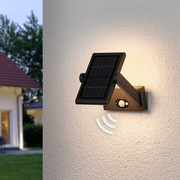 Schwarze Solar-Außenwandleuchte mit Bewegungsmelder und warmweißem Licht, montiert an einer hellen Hauswand.