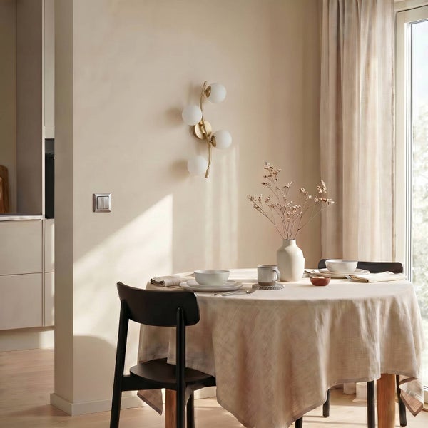 Moderne Wandleuchte mit vier Glaskugeln und Messinggestell in einem hellen Esszimmer mit gedecktem Tisch.
