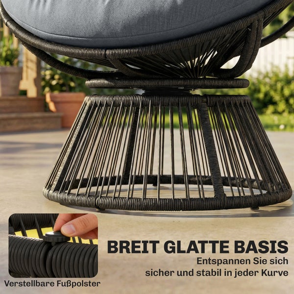 Schwarzer Papasan-Sessel aus Geflecht mit grauem Polster auf einer hellen Holzterrasse mit Beistelltisch und Pflanzen.