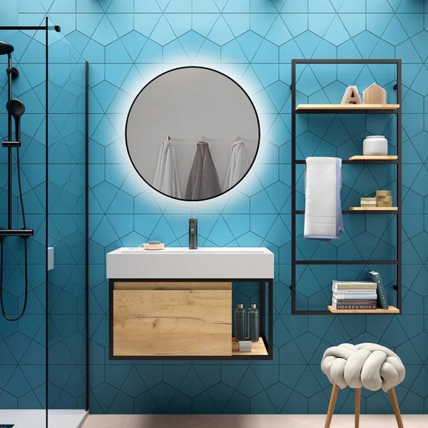 Modernes Badezimmer mit blauen geometrischen Fliesen, rundem beleuchtetem Spiegel, weißem Waschtisch auf Holzunterschrank und schwarzem Regal.