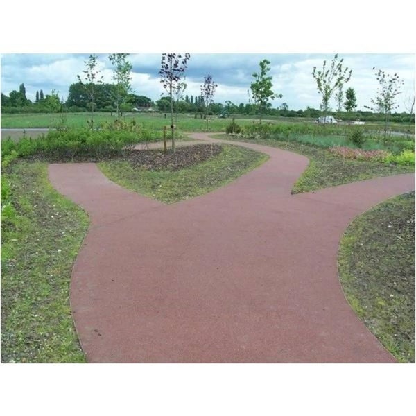 Verzweigter roter Gartenweg aus gebundenem Material in einer weitläufigen Grünanlage mit Rasen und jungen Bäumen.